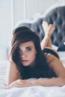 schoonheid in bed. mooi jong vrouw in zwart lingerie op zoek Bij camera terwijl aan het liegen in bed foto