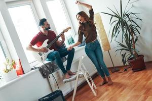 zorgeloos jong Mens in gewoontjes kleding spelen de gitaar terwijl zijn aantrekkelijk vriendin dansen foto