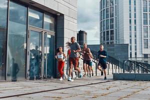 vol lengte van jong mensen in sport- kleding jogging terwijl oefenen Aan de trottoir buitenshuis foto