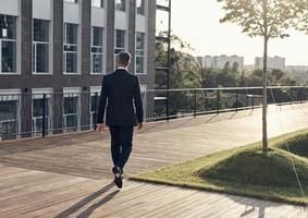 vol lengte achterzijde visie van Mens in vol pak wandelen in de buurt kantoor gebouw buitenshuis foto