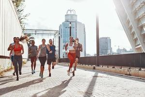 vol lengte van jong mensen in sport- kleding jogging terwijl oefenen Aan de trottoir buitenshuis foto