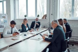 collega's in elegant formele kleding gebruik makend van modern technologieën en bespreken iets terwijl werken in de kantoor foto