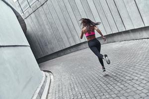 sport is de manier van haar leven. vol lengte achterzijde visie van jong vrouw in sport- kleding jogging terwijl oefenen buitenshuis foto