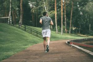 beginnend dag van ochtend- joggen. vol lengte achterzijde visie van jong Mens in sport- kleding jogging in park foto