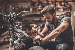 deze fiets zou moeten worden perfect. zelfverzekerd jong Mens repareren motorfiets in reparatie winkel foto