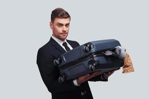 hoe naar transactie met deze bagage mooi zo op zoek jong Mens draag- vol over- Ingepakt koffer terwijl staand tegen grijs achtergrond foto