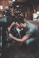 werken in zijn garage. zelfverzekerd jong Mens repareren motorfiets in de buurt zijn garage foto