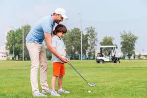 sharing met golf beleven. vrolijk jong Mens onderwijs zijn zoon naar Speel golf terwijl staand Aan de golf Cursus foto