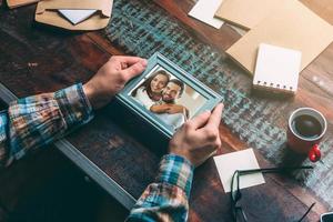 mooi zo herinneringen. detailopname top visie beeld van Mens Holding afbeelding kader terwijl zittend Bij de rustiek houten tafel foto