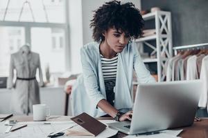 in tintje met klanten. mooi jong Afrikaanse vrouw werken gebruik makend van computer terwijl staand in werkplaats foto