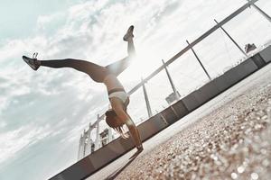 elke dag gevulde met sport. vol lengte van modern jong vrouw in sport- kleding aan het doen handstand terwijl oefenen buitenshuis foto