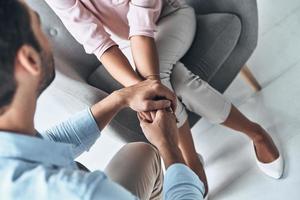 totaal in liefde. dichtbij omhoog top visie van jong paar Holding handen terwijl zittend binnenshuis foto