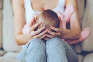 schat in haar handen. dichtbij omhoog een deel van jong vrouw Holding baby meisje Aan haar knieën terwijl zittend Aan de bankstel foto