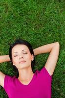 gevoel ontspannen en vredevol. top visie van mooi jong vrouw slapen terwijl Holding handen achter hoofd en aan het liegen Aan de groen gras foto