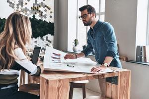 bespreken strategie. twee jong modern bedrijf mensen in slim gewoontjes slijtage gebruik makend van blauwdruk terwijl werken in de creatief werken ruimte foto