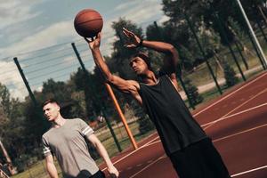 klaar naar schieten. twee jong mannen in sport- kleding spelen basketbal terwijl uitgeven tijd buitenshuis foto