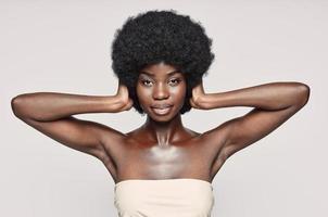 portret van mooi jong Afrikaanse vrouw aan het bedekken oren met handen terwijl staand tegen grijs achtergrond foto
