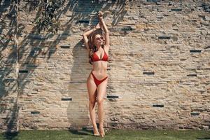 vol lengte van aantrekkelijk jong vrouw in bikini poseren terwijl staand buitenshuis foto