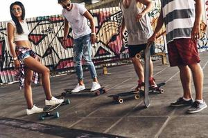 klaar naar reeks uit. groep van jong modern mensen met skates hangende uit samen buitenshuis foto