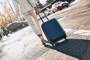 in een haast je. dichtbij omhoog achterzijde visie van jong vrouw trekken bagage terwijl wandelen buitenshuis foto