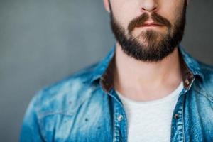 baard is zijn stijl. bijgesneden beeld van jong Mens vervelend overhemd terwijl staand tegen grijs achtergrond foto