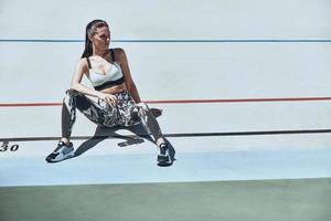 nemen een time-out. mooi jong vrouw in sport- kleding op zoek weg terwijl zittend Aan de rennen bijhouden buitenshuis foto