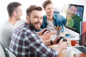 werk moeilijk Speel moeilijk. drie jong mannen spelen computer spellen terwijl zittend Bij de bureau in de kantoor foto