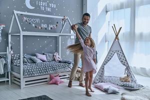 gaan gek samen. vol lengte van vader en dochter Holding handen en glimlachen terwijl dansen in slaapkamer foto