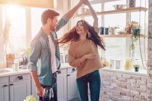 in liefde. mooi jong paar in gewoontjes kleding dansen en glimlachen terwijl staand in de keuken Bij huis foto