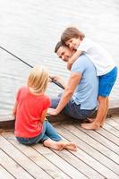 uitgeven Super goed tijd samen. gelukkig vader visvangst met zijn kinderen terwijl zittend Bij de oever van de rivier samen foto