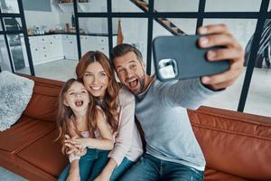 speels jong familie glimlachen en maken selfie terwijl uitgeven tijd Bij huis foto