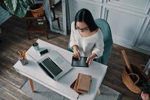 een ander deadline. top visie van mooi jong vrouw werken gebruik makend van digitaal tablet terwijl zittend in huis kantoor foto