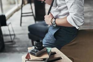 zijn favoriete hobby. detailopname van jong Mens in wit overhemd en bretels leunend Aan de sofa met foto camera De volgende naar hem