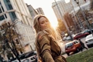 aantrekkelijk jong glimlachen vrouw op zoek Bij camera terwijl staand buitenshuis foto