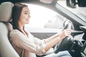 het rijden in de omgeving van stad. jong aantrekkelijk vrouw glimlachen en op zoek Rechtdoor terwijl het rijden een auto foto