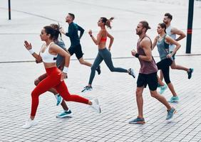 vol lengte van jong mensen in sport- kleding jogging terwijl oefenen Aan de trottoir buitenshuis foto