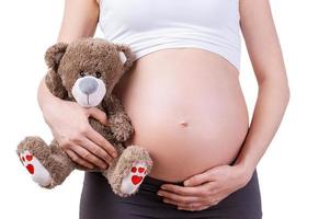 zwanger vrouw met teddy beer. bijgesneden beeld van zwanger vrouw Holding teddy beer terwijl staand geïsoleerd Aan wit foto