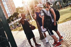 leven is beter met vrienden. groep van jong mannen in sport- kleding gebaren en glimlachen terwijl staand buitenshuis foto