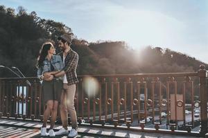 Super goed datum. vol lengte van mooi jong paar omarmen en op zoek Bij elk andere terwijl staand Aan de brug buitenshuis foto