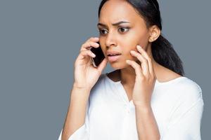 slecht nieuws over- de telefoon. depressief jong Afrikaanse vrouw pratend Aan de mobiel telefoon en aanraken gezicht met hand- terwijl staand tegen grijs achtergrond foto