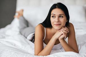 dromen over hem. jong vrouw op zoek weg en glimlachen terwijl aan het liegen Aan de bed Bij huis foto