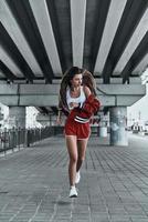 genieten van haar rennen. vol lengte van aantrekkelijk jong vrouw in sport kleding op zoek weg terwijl rennen onder de brug buitenshuis foto