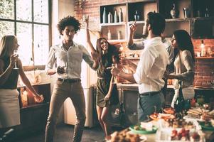 vrienden dansen. vrolijk jong mensen dansen en drinken terwijl genieten van huis partij Aan de keuken foto