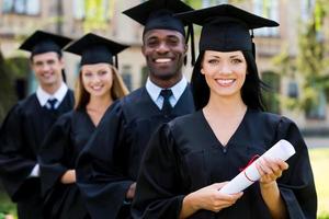 gelukkig afgestudeerden. vier college afgestudeerden staand in een rij en glimlachen foto