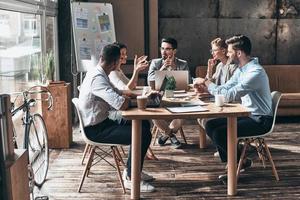 zelfverzekerd en geslaagd team. groep van jong modern mensen in slim gewoontjes slijtage bespreken bedrijf terwijl zittend in de creatief kantoor foto