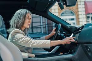 volwassen mooi vrouw in slim gewoontjes slijtage gebruik makend van globaal positionering systeem terwijl het rijden auto foto
