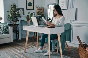 bezig werken dag. mooi jong vrouw werken gebruik makend van digitaal tablet terwijl zittend in huis kantoor foto