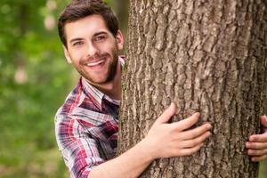 speels schoonheid in natuur. knap jong vrouw op zoek uit van de boom en glimlachen foto