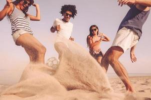 iedereen wil naar winnen. groep van vrolijk jong mensen spelen met voetbal bal Aan de strand foto