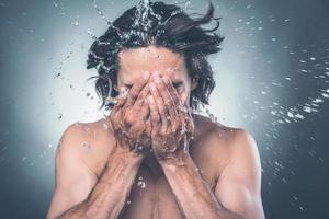 krijgen opgefrist. jong zonder shirt Mens het wassen gezicht met water spatten in de omgeving van hem foto